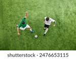 Aerial view. Two players in white and green uniforms battle for the ball on green lush playground. Concept of professional sport, championship, final match, movement. Ad