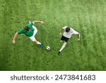 Aerial view. Two soccer players in attack position, fight for ball in motion on green lush playground. Concept of professional sport, championship, final match, movement. Ad