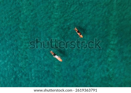 An aerial view of two surfers padding in turquoise water