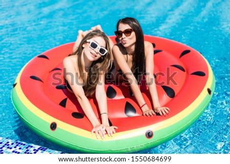 Aerial view of two womenlying on inflatable watermelon mattrass floating and relaxing in swimming pool