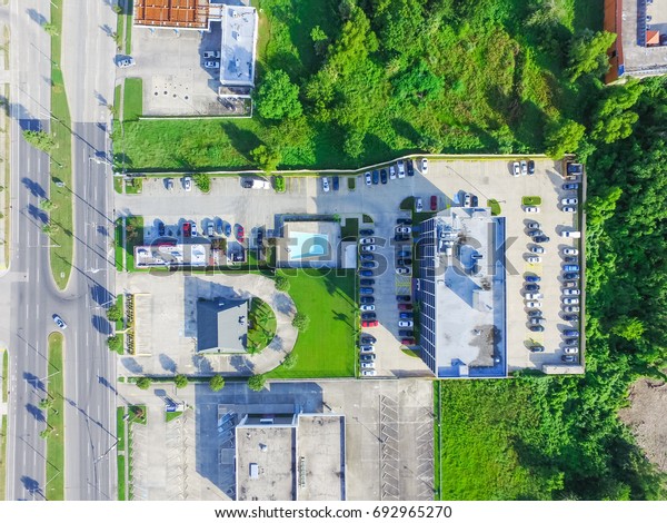 Aerial view of\
typical multi story hotel next to road with traffic, swimming pool,\
surrounded by green tree and rows of cars in parking lots in New\
Orleans, Louisiana, US.