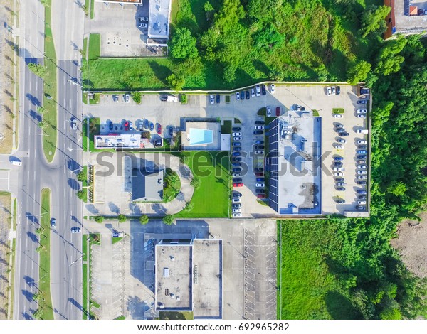 Aerial view of\
typical multi story hotel next to road with traffic, swimming pool,\
surrounded by green tree and rows of cars in parking lots in New\
Orleans, Louisiana, US.