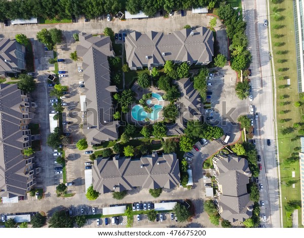 Aerial view of typical multi-level apartment\
building with swimming pool, surrounded by green garden and rows of\
cars in parking lots in Houston, Texas, US. Apartment complex next\
to road with traffic