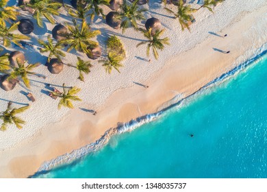 Aerial View Of Umbrellas, Palms On The Sandy Beach, People, Blue Sea With Waves At Sunset. Summer Holiday In Zanzibar, Africa. Tropical Landscape With Palm Trees, Parasols, White Sand, Ocean. Top View