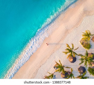 Aerial View Of Umbrellas, Palms On The Sandy Beach Of Indian Ocean At Sunset. Summer In Zanzibar, Africa. Tropical Landscape With Palm Trees, Parasols, Walking People, Blue Water, Waves. Top View