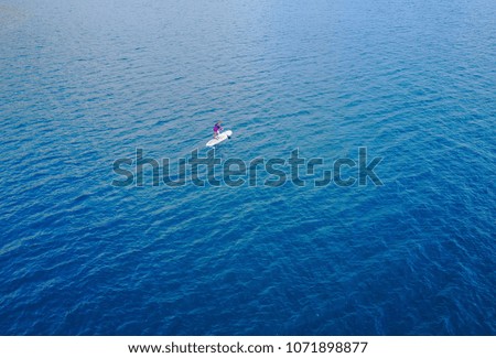 Aerial view of Unidentified women tourist paddling a surfboard to middle of the sea