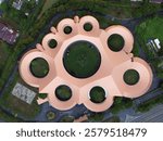 Aerial view of a uniquely designed building with a circular and curved layout, resembling a paw print. The structure features multiple circular openings and a central courtyard surrounded by greenery.