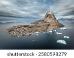 Aerial view of Uummannaq island during a sunny day with colorful houses, floating giant icebergs and dramatic clouds. Northwest Greenland, autonomous territory of Denmark. 