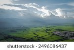 An aerial view of Valle del Cauca, Colombia, featuring lush green fields and distant mountains under dramatic clouds.