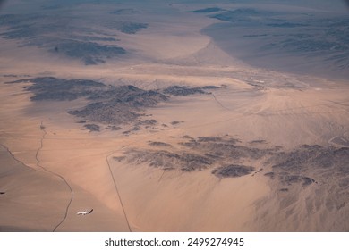 Aerial view of a vast desert landscape with scattered rocky outcrops and an airplane flying over, highlighting the stark beauty and expansive scale of the arid terrain.
 - Powered by Shutterstock