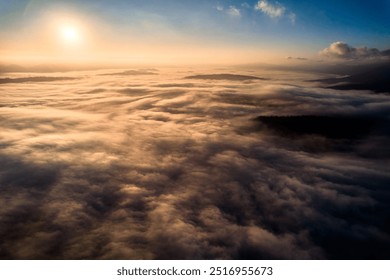 Aerial view of vibrant sunset over white dense clouds bathes in warm golden light, creating dreamlike landscape. Soft shadows play across undulating clouds, while distant landforms peek through mist. - Powered by Shutterstock