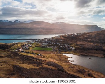 Aerial view of the village Eidi with snow-covered mountain range, football field and dramatic sky during sunset (Faroe Islands, Denmark, Europe) - Powered by Shutterstock