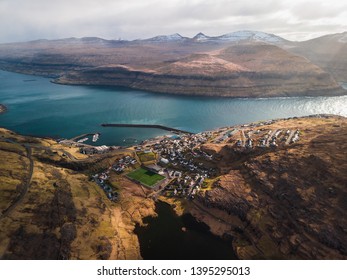 Aerial view of the village Eidi with snow-covered mountain range, football field and dramatic sky during sunset (Faroe Islands, Denmark, Europe) - Powered by Shutterstock