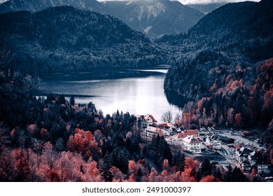 Aerial view of a village nestled in a valley surrounded by dense forest, with a glistening lake in the center. The village has buildings with red roofs, and the forest is transitioning into autumn col - Powered by Shutterstock