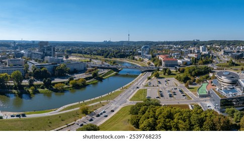 Aerial view of Vilnius, Lithuania, featuring the Neris River, lush greenery, modern buildings, and the distant Vilnius TV Tower under a clear blue sky. - Powered by Shutterstock