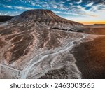 Aerial view of a volcanic landscape in Saudi Arabia, showcasing a dramatic volcano and expansive lava field. The rugged terrain features dark, solidified lava flows and striking geological formations 