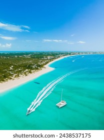 aerial view of wake boat and catamaran sailing on award winning grace bay, providenciales with island and long stretch of white sand beach in sight