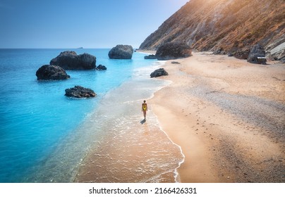 Aerial View Of Walking Young Woman On Empty Sandy Beach Near Sea With Waves At Sunset. Summer Vacation In Lefkada Island, Greece. Top View Of Sporty Girl, Blue Water, Mountain. Lifestyle And Travel