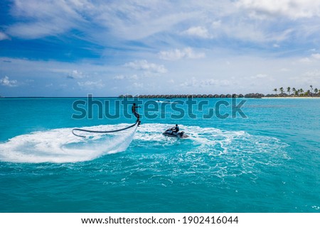 Aerial view of water extreme action sport, summer sea, close to luxury tropical resort . Fly board in ocean lagoon, freedom fun as summer recreational activity. Flyboard view from drone