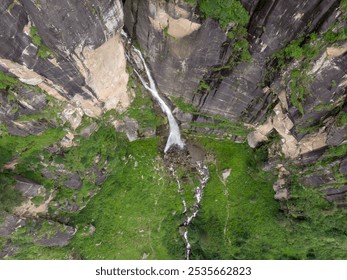 Aerial view of a waterfall cascading down a rocky cliff into lush greenery. - Powered by Shutterstock