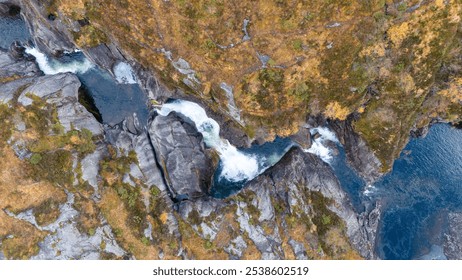 Aerial view of a waterfall cascading through rocky terrain surrounded by autumn foliage. - Powered by Shutterstock