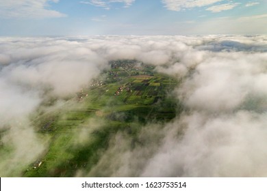 Aerial View Of White Clouds Above A Town Or Village With Rows Of Buildings And Curvy Streets Between Green Fields In Summer. Countryside Landscape From Above.