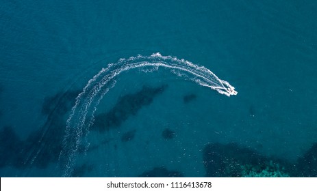 Aerial view of a white motorboat running on the azure waters of the Tyrrhenian Sea. On his trip near the coast the boat leaves a white trail in the waves of the sea.