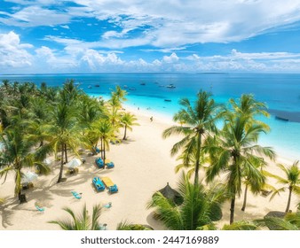 Aerial view of white sandy beach with palm trees, sunbeds, umbrellas, yachts, boats, blue ocean, sky with clouds at sunset. Summer in Kendwa, Zanzibar island. Tropical landscape. Clear sea. Top view - Powered by Shutterstock