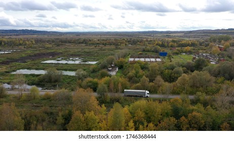 Aerial View Of White Truck With Cargo Semi Trailer Moving On Road In Direction Of Loading Warehouse Area. Large Delivery Truck Is Moving. Aerial Shot Of Lorry On Road In Beautiful Countryside.