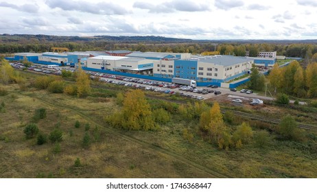 Aerial View Of White Truck With Cargo Semi Trailer Moving Near Loading Warehouse Area. Large Delivery Truck Is Moving. Aerial Shot Of Lorry On Road In Beautiful Countryside.