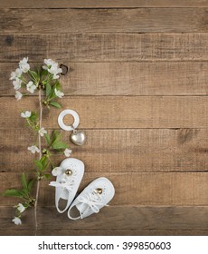 Aerial View of White Vintage Baby Shoes with Antique Teething Ring and White Flowers on Horizontal Rustic Wood Board Background with room or space for copy, text, your words, Vertical Warm toned