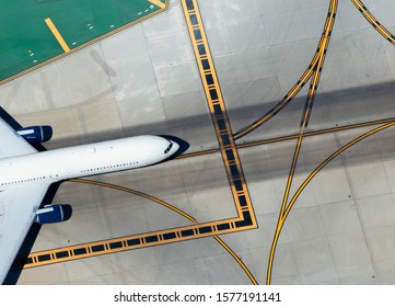 Aerial view of widebody aircraft taxiing with multiple yellow lines for traffic pattern on tarmac as background. International airport navigation before journey. Wide crop with space for text.