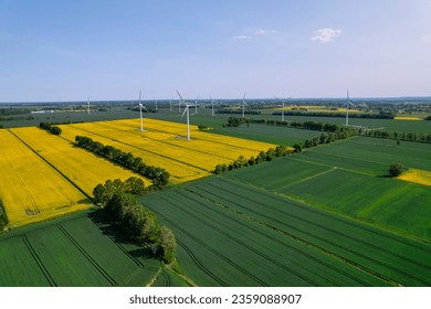 Aerial view Wind turbine on grassy yellow farm canola field against cloudy blue sky in rural area. Offshore windmill park with clouds in farmland Poland Europe. Wind power plant generating electricity - Powered by Shutterstock