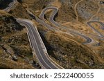 Aerial view of a winding mountain road with cyclists. Road is surrounded by dry grass and rocky terrain. Sportsmen training hard on bicycle outdoors.Sports motivation. Cycling professional group ride.