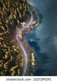 Aerial view of winding road with blue lake. Great road trip trough the dense woods. Aerial view with green pine foliage in Bucegi Mountains, Romania