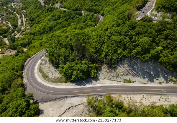 Aerial view of\
winding road from the high mountain pass. Great road trip trough\
the dense woods. Birds eye\
view.