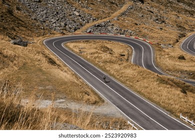 Aerial view of winding road through a mountain passWoman cyclist pedaling up the hill, while the road curves and twists around the rugged landscape.Cycling through stunning Romanian mountain landscape - Powered by Shutterstock