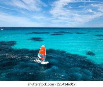 Aerial view of windsurfer on blue sea at sunny summer day. Windsurfing. Extreme sport and vacation. Top view of man on windsurfer board, waves, clear azure water in Sardinia, Italy. Tropical landscape - Powered by Shutterstock