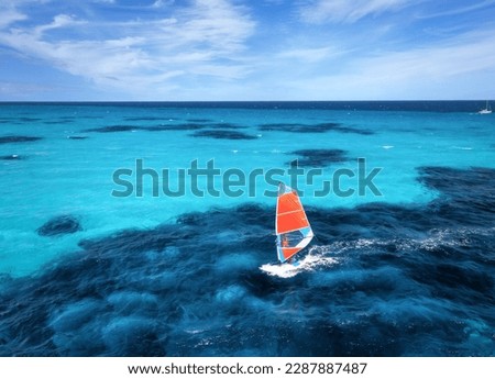 Aerial view of windsurfer on blue sea at sunny summer day. Windsurfing. Extreme sport and vacation. Top view of man on windsurfer board, waves, clear azure water in Sardinia, Italy. Tropical landscape