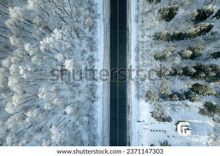 Aerial view of winter landscape with snow covered woods and black asphalt forest road on cold wintry day