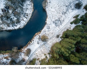 Aerial view of winter river Merkys near Merkine, Lithuania. Surrounded by pine tree forest, with snow on the grass.