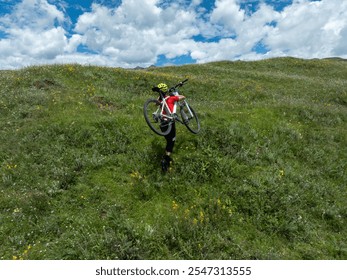 Aerial view of woman cyclist carrying a mountain bike climbing up to beautiful flowering grassland mountain top - Powered by Shutterstock