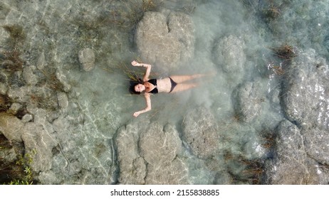 Aerial View Of A Woman With Long Hair And A Black Bikini Floating Bacalar Lagoon And Blue Cenote, Near Cancun, In Riviera Maya, Mexico. Turquoise Blue Shallow Water And Beautiful Place To Go And Relax