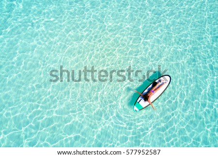 Aerial view of a woman on a surfboard in the turquoise waters of the Maldives