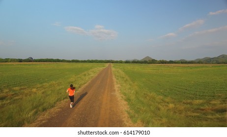 Aerial view of woman running on a rural road during sunset in the mountains - Powered by Shutterstock