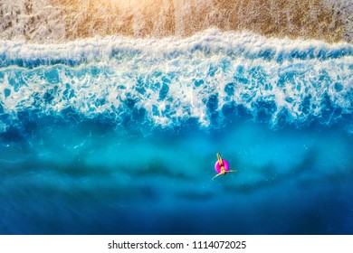 Aerial view of woman swimming on the pink swim ring in the sea in the morning in Europe. Summer landscape with girl, beach, blue water, beautiful waves at sunrise. Top view. Travel and holiday. Resort