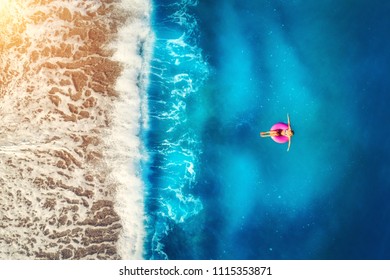Aerial view of woman swimming on the pink swim ring in the transparent sea and beautiful waves in Europe. Summer landscape with girl, beach, blue water at sunset. Top view. Travel and holiday. Resort