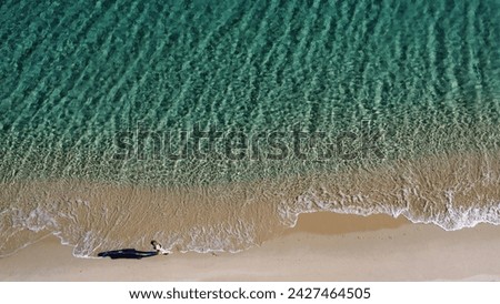 Aerial view of woman walking on the sandy beach with ocean waves braking on the coast. Summer vibes. Sardinia. Travel concept.
