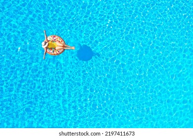 Aerial view of a woman in yellow swimsuit lying on a donut in the pool