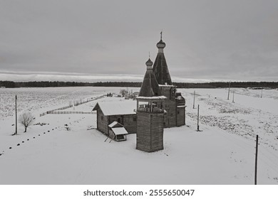 Aerial view of the wooden church and bell tower in winter against the backdrop of snow and gray sky. Russian village - Powered by Shutterstock